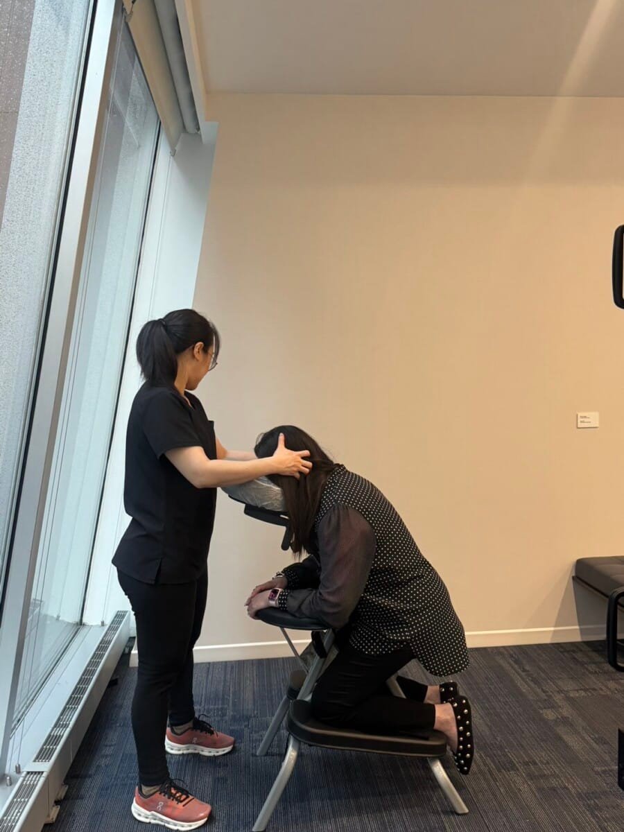 Gallery 13 Massage therapist delivering office massage in a modern NYC workspace, employee seated in ergonomic chair.