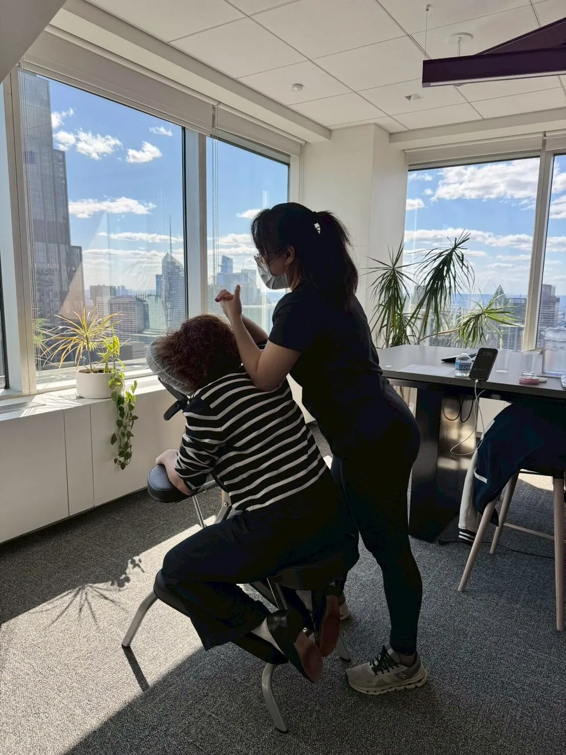 Therapist giving a seated massage beside large windows in a New York office